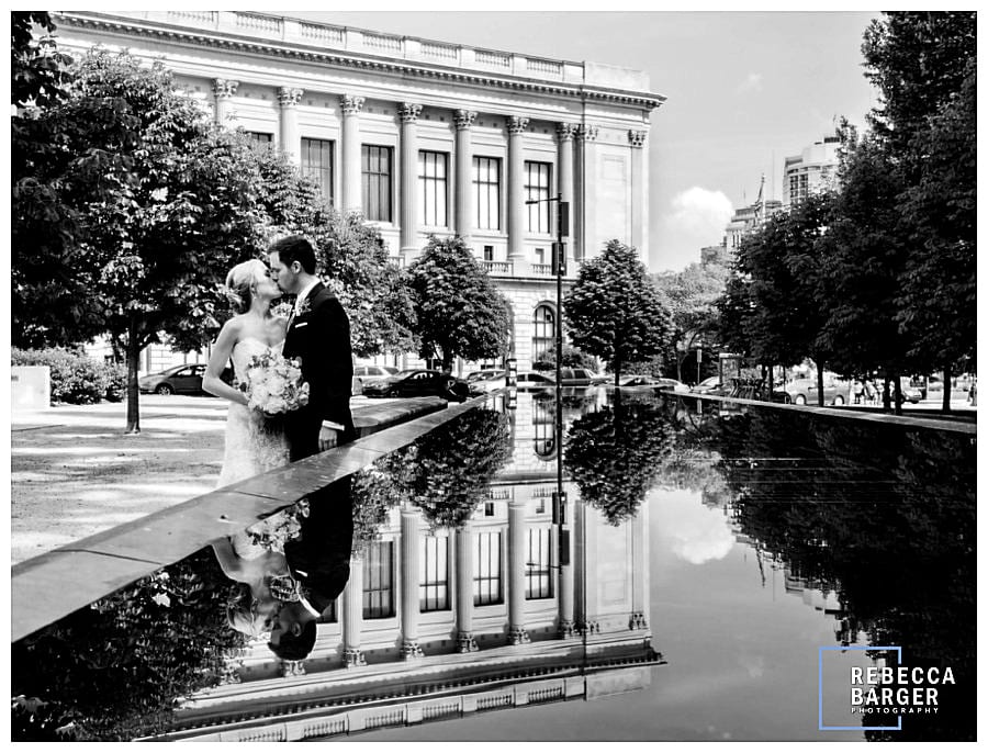 Lauren and James share a wedding day kiss as the Philadelphia Free Library is reflected in a fountain pool.